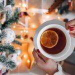 photo of a person holding a cup of tree with a christmas tree lit up in the background